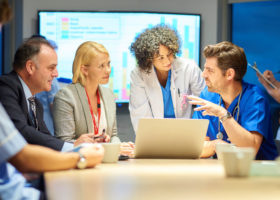 a mixed group of healthcare professional and business people meet around a conference table